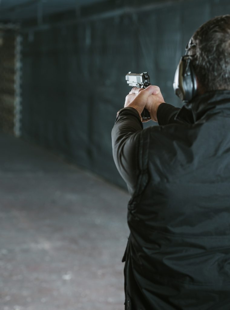 rear-view-of-man-aiming-gun-at-target-in-shooting-range.jpg